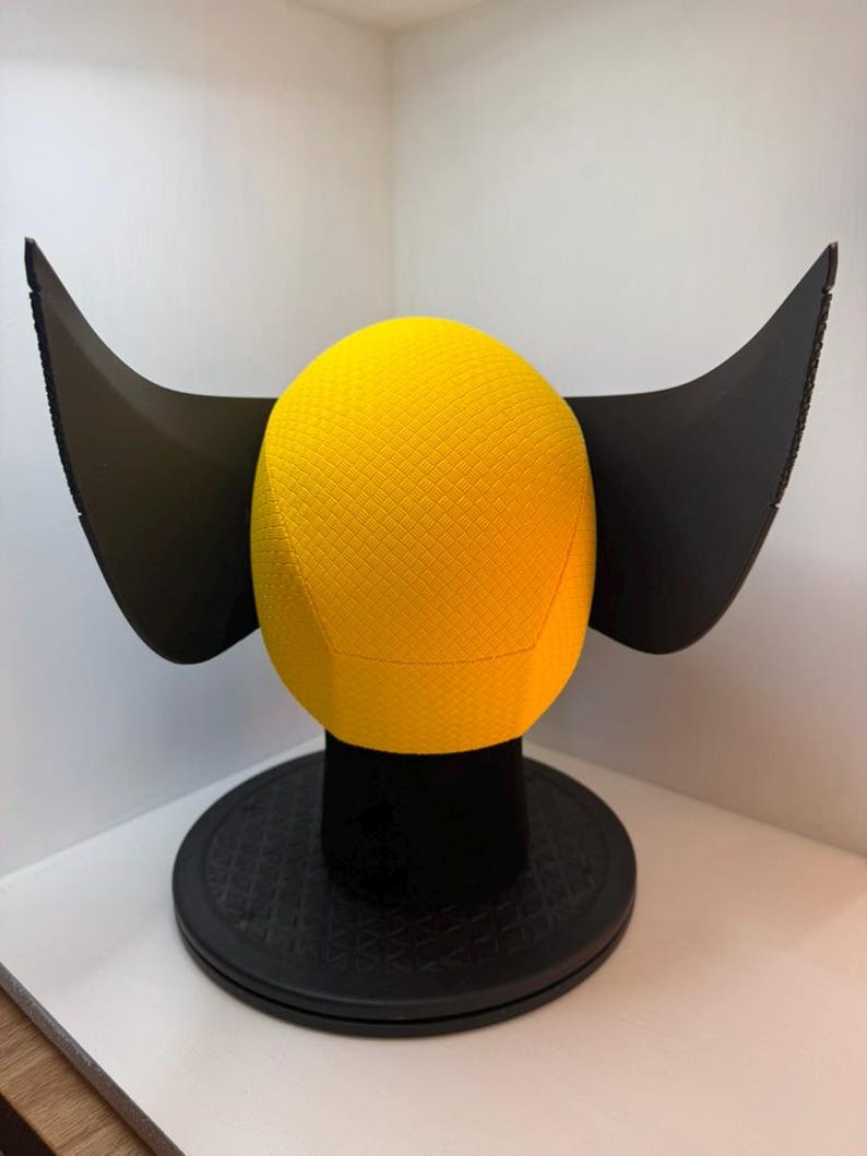 Peut inclure: Une sph&egrave;re jaune textur&eacute;e avec des extensions noires en forme d'ailes, mont&eacute;e sur une base circulaire noire. La sph&egrave;re pr&eacute;sente un motif en losange. L'objet est une pi&egrave;ce d&eacute;corative, peut-&ecirc;tre une sculpture ou un objet d'exposition unique.
