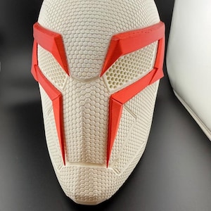 Peut inclure: Un masque blanc texturé avec des détails rouges. Le masque présente un motif en nid d'abeille et des formes géométriques rouges autour des yeux et du nez. Le design est futuriste, idéal pour le cosplay ou les costumes.
