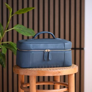 Large leather makeup bag in teal color with gold zippers. Travel cosmetics organizer with top handle and protective feet.