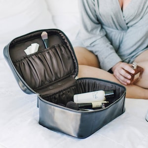 May include: A black leather travel makeup bag with multiple compartments and a zipper closure. The bag is open and contains various toiletries and makeup brushes.