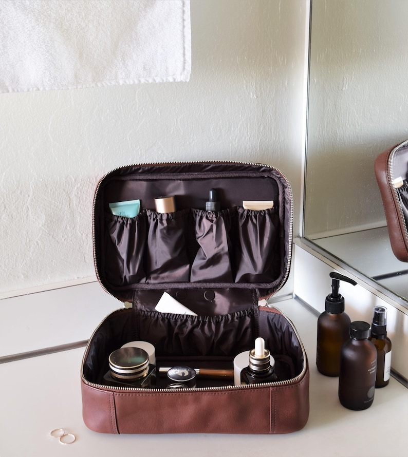 Leather wash bag on bathroom counter, organized elastic pockets holding toiletries — wipe clean lining, open lifestyle view