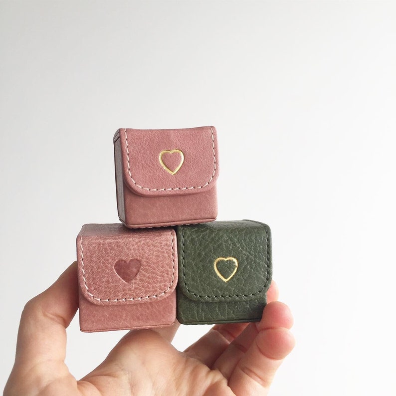 May include: Three small square boxes with heart-shaped designs. Two boxes are pink with gold hearts and one box is green with a gold heart.