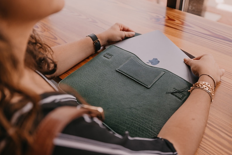 Aloe green full-grain leather laptop sleeve with interior business card pocket and magnetic closure—MacBook being inserted, slim protective case