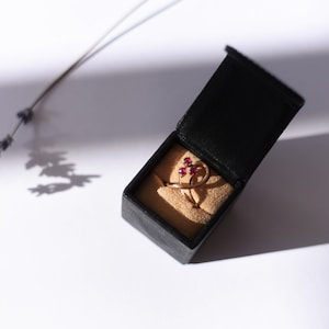 May include: A gold ring with three ruby stones set in a delicate, swirling design. The ring is displayed in a black velvet ring box.
