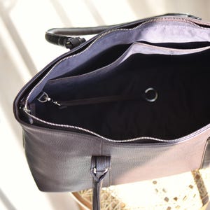 May include: Open view of a brown leather tote bag with a silver zipper and handles. The interior is black with pockets and a silver ring. The bag is sitting on a light-colored surface.