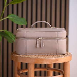 Warm crème or beige pebbled full grain leather make up storage or vanity organizer with gold zippers.