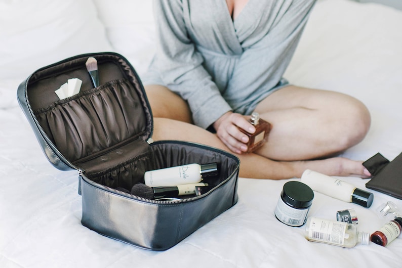 May include: A black leather travel makeup bag with multiple compartments and a zipper closure. The bag is open and contains various toiletries and makeup brushes.