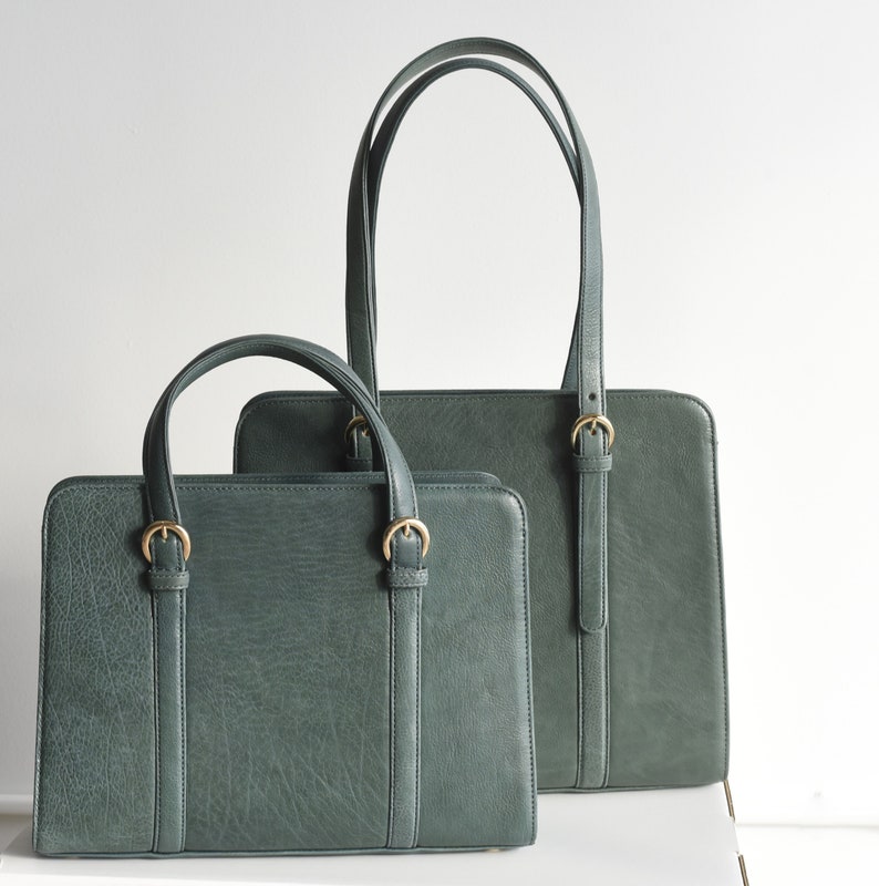 Two Aloe green leather bags with gold buckles. The larger Shoulder bag is behind the smaller Handbag. Both bags have a structured shape and are made of full grain leather.