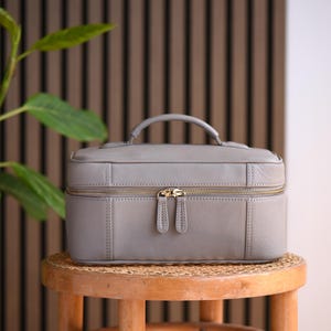 Warm gray soft pebbled leather cosmetics case with gold zippers and top handle.
