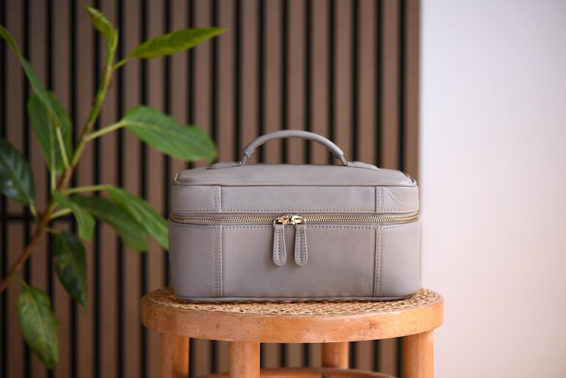 Warm gray soft pebbled leather cosmetics case with gold zippers and top handle.