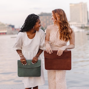 Lifestyle photo of two women holding leather laptop sleeves— Aloe green and Coffee brown—personalized monograms, professional work accessories