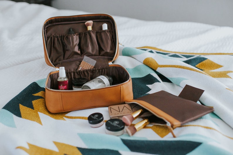 Leather cosmetics and toiletry case on bed with detachable magnetic zip pouch — organized storage for travel essentials