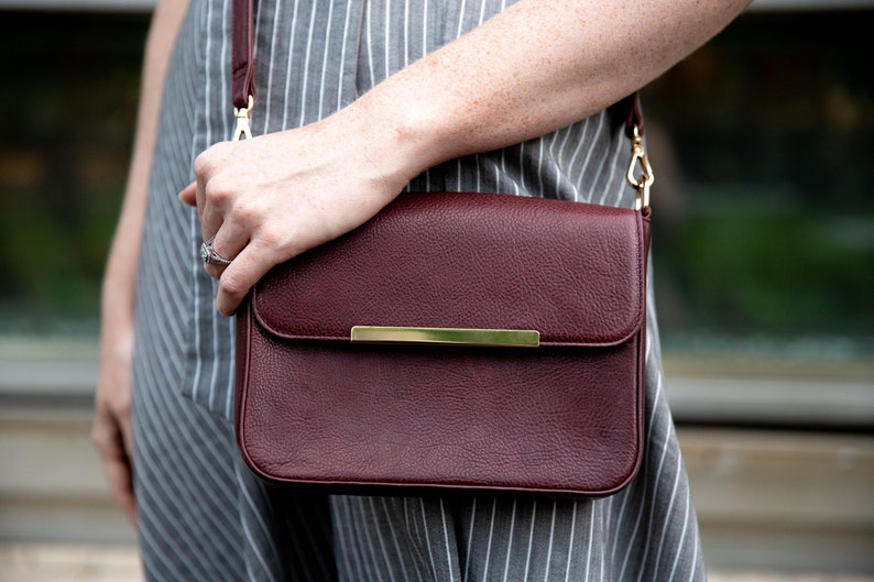May include: A burgundy leather crossbody bag with a gold strap and a gold accent on the front flap.