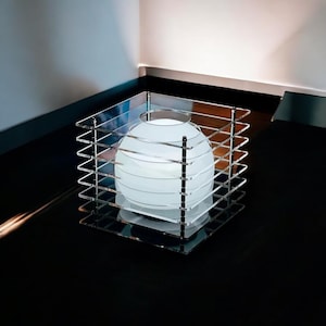 May include: A contemporary table lamp with a frosted glass globe inside a clear acrylic cube. The lamp has a minimalist design with a spherical light source and a geometric, transparent frame. The lamp is on a black surface.