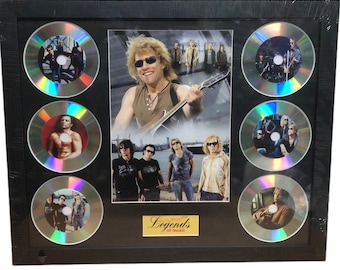 May include: Framed display featuring a central image of a musician with a guitar, surrounded by six CDs. The CDs and central image showcase the musician and band members. The frame is black, and a gold plaque at the bottom reads "Legends of music."