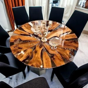 Puede incluir: Una mesa de comedor redonda con un diseño único. La superficie presenta un patrón de vetas de madera natural encapsulado en resina transparente. Seis sillas negras rodean la mesa. Una lámpara de araña decorativa cuelga encima.