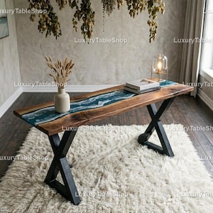 Puede incluir: Una mesa de madera hecha a mano con un diseño de río de resina azul. La mesa tiene un acabado de madera oscura, patas de metal negro y mide aproximadamente 152 cm de largo. Un jarrón con flores secas y libros están sobre la mesa.