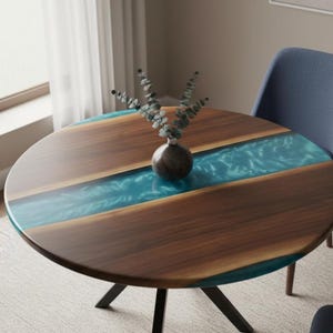 Puede incluir: Una mesa redonda de madera con un diseño de río de resina epoxi azul. La mesa tiene una veta de madera marrón oscuro y un acabado brillante. Un pequeño jarrón con vegetación se encuentra sobre la mesa. La mesa está sostenida por patas de metal negro.