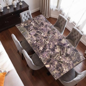 Puede incluir: Una mesa de comedor rectangular con una llamativa tapa de piedra de amatista. Seis sillas grises tapizadas rodean la mesa. La habitación cuenta con pisos de madera oscura y un gabinete de madera oscura con jarrones decorativos. La mesa mide unos 200 cm de largo.