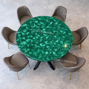 Op de afbeelding: Een ronde eettafel met een levendig groen, geometrisch patroon. De tafel wordt omringd door zes grijze, gestoffeerde stoelen met goudkleurige poten. De tafel heeft een zwarte basis. De tekst "Luxury Table Shop" is zichtbaar.