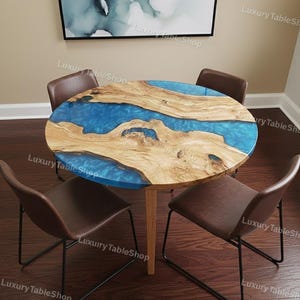 Puede incluir: Una mesa redonda de madera con un centro de resina azul y bordes de madera natural, rodeada de cuatro sillas marrones con patas de metal negro. La mesa tiene unos 100 cm de diámetro.