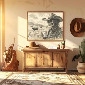 May include: A framed black and white print of a cowboy skeleton in a hat, holding a cup, with cows in the background. A brown cowboy hat hangs on the wall. A wooden cabinet holds a hat, books, and small potted plants. A leather bag leans against the wall.