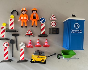 May include: A collection of toy construction equipment and figures. Includes two orange-clad construction workers, road signs, traffic cones, a portable toilet, a wheelbarrow, and a yellow compactor. The signs feature speed limits and warning symbols.