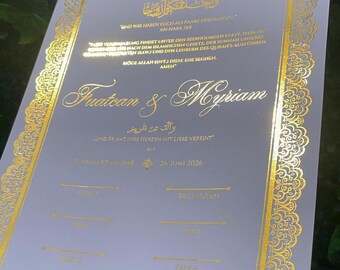 May include: A white wedding contract document featuring an ornate gold foil border and gold foil text. The document includes Arabic calligraphy, German text, the names Fuatcan & Myriam, and lines for signatures labeled Braut, Bräutigam, and Zeuge.