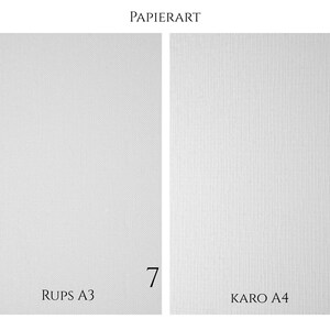 May include: Two white paper sheets labeled PAPIERART. The left sheet is marked RUPS A3 with the number 7. The right sheet features a vertical lined texture and is marked KARO A4 with the number 8. Both are rectangular and white.