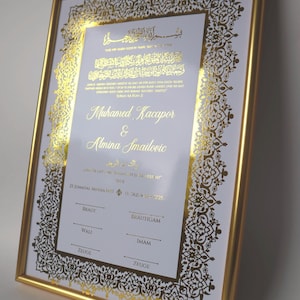 Könnte beinhalten: Eine rechteckige Hochzeitsurkunde in einem goldenen Rahmen mit arabischer Kalligrafie und deutschem Text in Goldfolie. Das Dokument enthält die Namen Muhamed Kacapor und Almina Smailovic sowie Zeilen für Unterschriften: Braut, Brautigam, Wali, Imam, Zeuge.