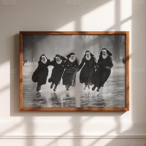 May include: Black and white framed print featuring five nuns ice skating, holding hands, and smiling. The image is set in a winter landscape, with the nuns wearing traditional habits and skates. The frame is a warm brown color.