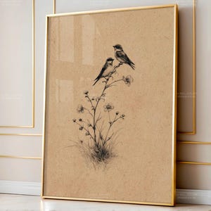 Puede incluir: Una impresión enmarcada con una detallada ilustración en blanco y negro de dos pájaros posados en una rama floreciente. La obra de arte está sobre un fondo marrón claro y encerrada en un marco dorado, creando una estética vintage.