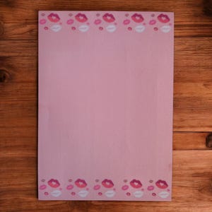 Op de afbeelding: Een roze vel briefpapier met een rand van herhaalde lipontwerpen in roze en witte tinten. Het papier is rechthoekig en heeft een glad oppervlak, geschikt voor het schrijven van brieven of notities.