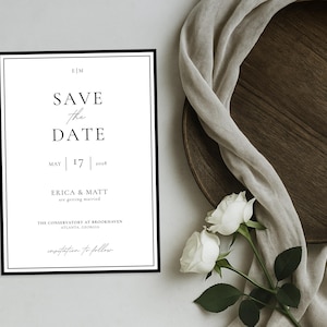 Peut inclure: Une invitation de mariage minimaliste avec une bordure noire, affichant le texte "SAVE THE DATE" et la date du 17 mai 2028. L'invitation est accompagnée de roses blanches, d'une assiette en bois et d'un tissu drapé.