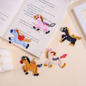 May include: Embroidered horse patches in various colors, including pink, blue, black, and tan. Each patch features a unique design, such as hearts, apples, and the word "Love" or the number "2026". These patches are ideal for adding a decorative touch to clothing or accessories.