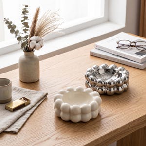 May include: A white ceramic mug with a black handle and the text "But First, Coffee" in a black, handwritten-style font. The mug is on a white surface.