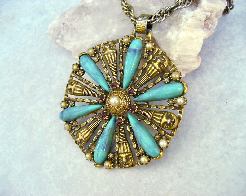 May include: A gold tone pendant necklace with a turquoise and pearl flower design. The pendant features a circular design with turquoise stones and pearls around a central pearl.