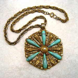 May include: A gold tone necklace with a large pendant featuring a turquoise and red stone design. The pendant is shaped like a flower with a central pearl.