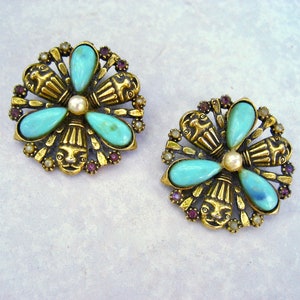 May include: A pair of gold tone earrings featuring turquoise and purple stones. The earrings are shaped like flowers with a central pearl.