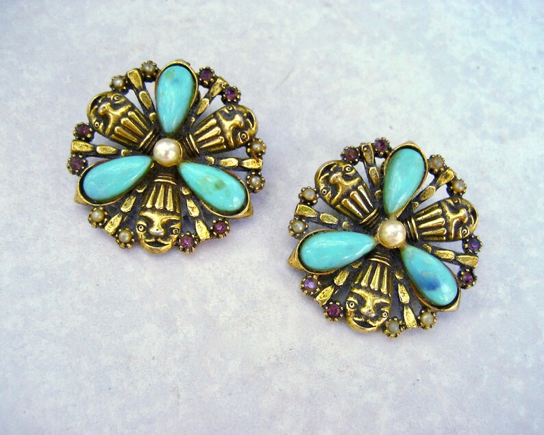 May include: A pair of gold tone earrings featuring turquoise and purple stones. The earrings are shaped like flowers with a central pearl.