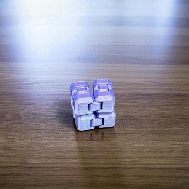 K&ouml;nnte beinhalten: Ein helllila Infinity-Cube-Spielzeug, das aus mehreren verbundenen Bl&ouml;cken besteht. Das Spielzeug besteht aus Kunststoff und liegt auf einer Holzoberfl&auml;che. Der W&uuml;rfel ist so konzipiert, dass er auf verschiedene Weise manipuliert und gefaltet werden kann.