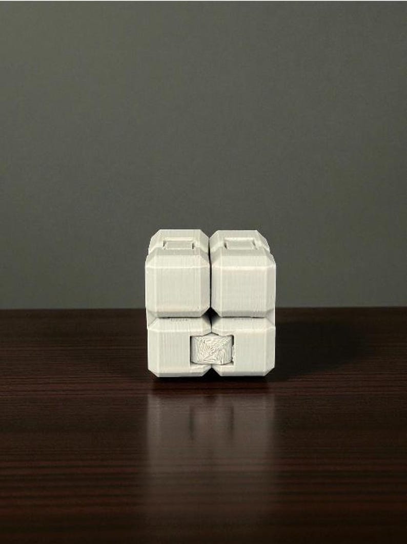 K&ouml;nnte beinhalten: Ein wei&szlig;es, geometrisches Zappelspielzeug mit einem w&uuml;rfelf&ouml;rmigen Design. Das Spielzeug besteht aus mehreren rechteckigen Bl&ouml;cken, die miteinander verbunden sind. Die Bl&ouml;cke haben eine strukturierte Oberfl&auml;che und sind symmetrisch angeordnet.
