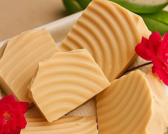 May include: Five light brown, textured soap bars on a white tray, with red flowers and green aloe vera leaves. The soap has a wavy pattern. The background is a light tan colour.