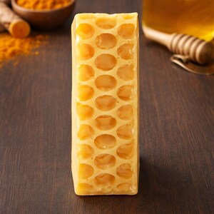 May include: A block of honeycomb with a distinctive hexagonal cell pattern. The honeycomb is a pale yellow hue, set against a dark brown wooden backdrop. Turmeric, honey, and a honey dipper are visible in the background.