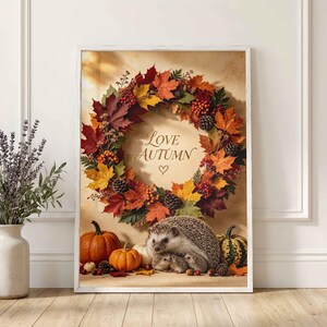 May include: A rectangular wall art print featuring a wreath of colourful autumn leaves, pinecones, and berries surrounding the text Love Autumn with a heart symbol. Below the wreath are three hedgehogs, orange pumpkins, and a green striped gourd.