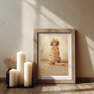 May include: A framed print with a Cockapoo dog and the text "Life is Better With a Cockapoo." The frame is light brown wood. Three white candles and a small vase with dried flowers are in front of the frame, adding to the decor.