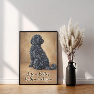 Puede incluir: Impresión enmarcada con un perro Cockapoo negro sentado y mirando hacia la derecha. La impresión tiene el texto "Life is Better With a Cockapoo" en cursiva con corazones rojos. Un jarrón negro con plantas altas y plumosas está a la derecha.