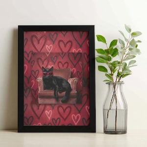 Può includere: Stampa artistica incorniciata con un gatto nero con occhiali da sole a forma di cuore, seduto in una poltrona. Lo sfondo è un motivo di cuori rossi. La stampa è in una cornice nera, con un vaso di vetro e vegetazione a destra.