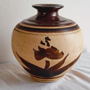 May include: A handcrafted ceramic vase with a rounded body and a narrow neck. The vase features a beige base with brown floral design and dark brown accents. The vase is approximately 8 inches tall.