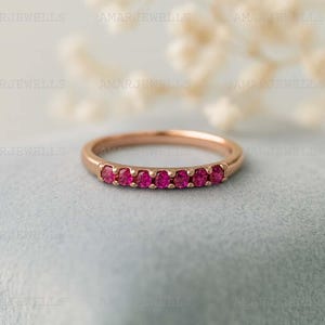 May include: A rose gold ring featuring a row of seven vibrant, round-cut rubies. The gemstones are set closely together, creating a continuous line of rich red color. The ring has a delicate band, showcasing the gemstones prominently.